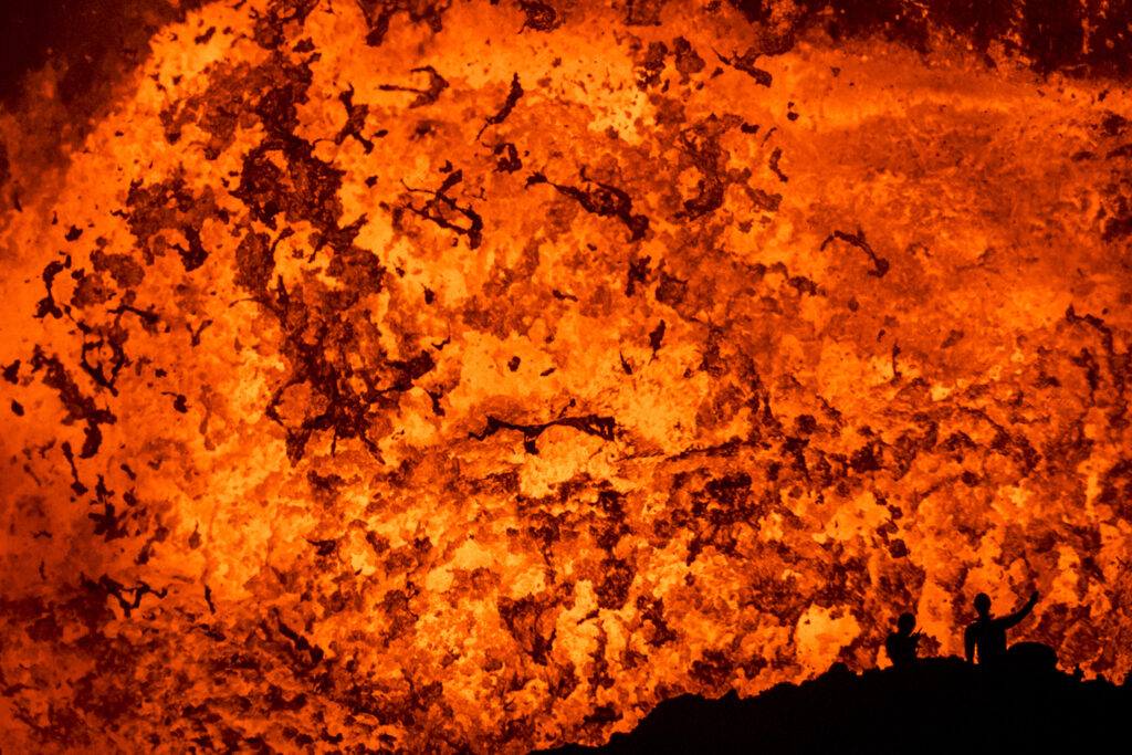 Der französische Wissenschaftler Thomas Boyer und der deutsche Alpinist Sebastian Hofmann stehen am Rand des 1200 Grad heißen Lava Sees des Benbow Vulkanes. Thomas Boyer misst die Temperatur mit einem Spezialthermometer. Diese Messungen kann er nur nahe am Lava See ausführen, da sonst die vulkanischen Gase seine Ergebnisse verfälschen würden.