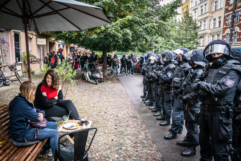 Europa, Deutschland, Berlin: Querdenker-Proteste in Berlin anlaesslich des Jahrestages zur Erstuermung der Treppe des Reichstagsgebaeudes. Die Demonstrationen ware im Vorfeld verboten worden, rund 5000 Teilnehmer waren dennoch in die Hauptstadt gekommen. Hier am Prenzlauer Berg sitzen Passanten in einem Café, die Polizei bildet eine Kette gegen die Querdenker auf der Strasse.

Europe, Germany, Berlin: Protests in Berlin on the occasion of the anniversary of the storming of the stairs of the Reichstag building. The demonstrations had been banned in advance, but around 5,000 participants had nevertheless come to the capital.